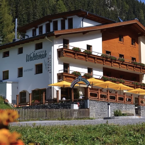 Das Hotel Waldesruh mit weißer Fassade, Holzbalkonen und gelben Sonnenschirmen an der Terrasse.