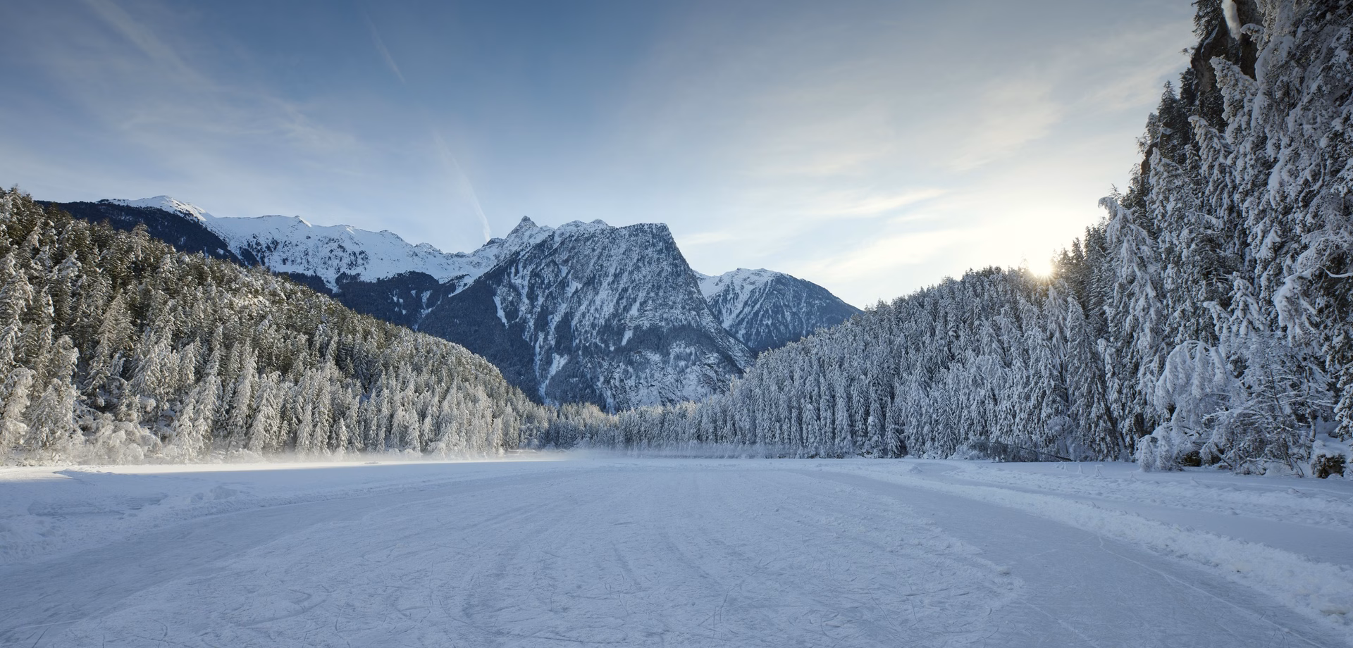 A snowy winter landscape with a frozen open area, forests and mountains near Ochsengarten in the Ötztal.