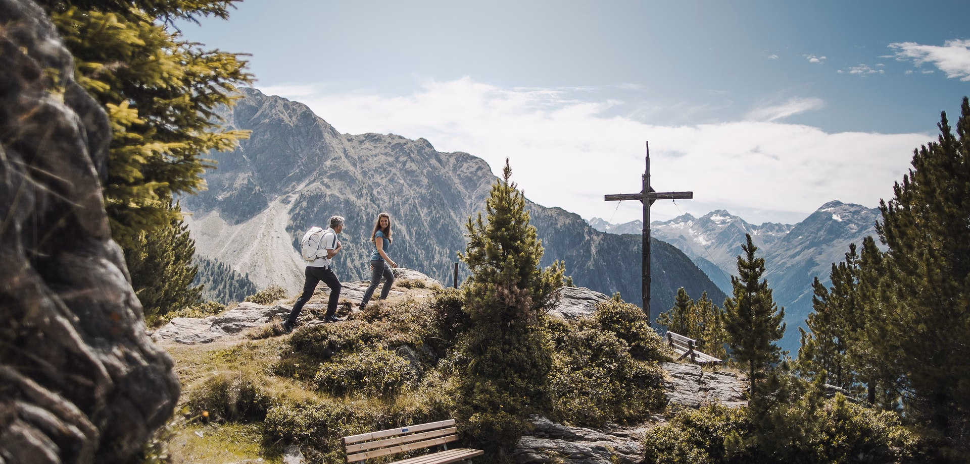 Two hikers stand on a rocky viewpoint overlooking the mountains in the Ötztal.