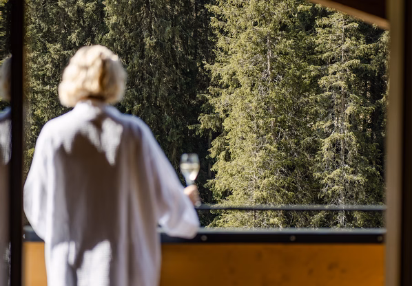 Wellnessbereich mit Blick ins Grüne Eine Person im Bademantel steht auf dem Balkon und blickt in den Wald.