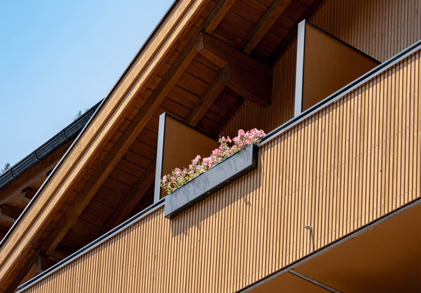 Hotelgebäude mit Holzbalkonen in Ochsengarten Die Fassade des Hotelgebäudes zeigt Holzverkleidung, Balkone und Blumenkästen unter dem Satteldach.