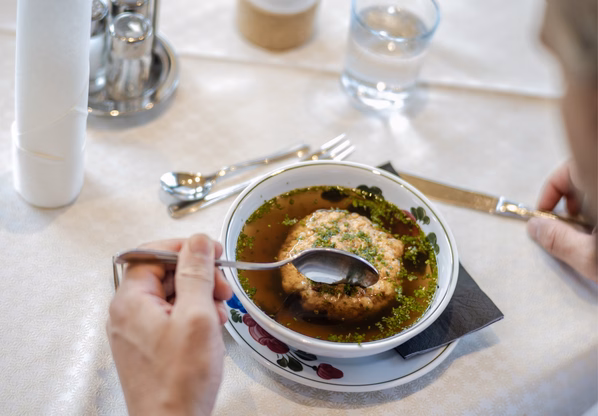Suppenteller im Hotelrestaurant Ochsengarten Eine Person löffelt eine klare Suppe mit Einlage an einem gedeckten Tisch.