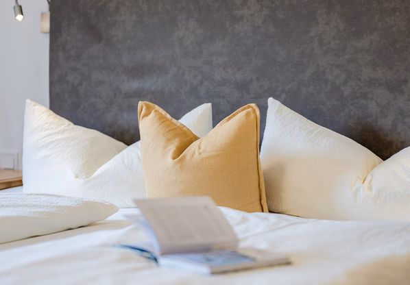 Hotelzimmer im Hotel Waldesruh mit Kopfkissen Ein aufgeschlagenes Buch liegt auf dem Bett vor mehreren weißen und gelben Kissen im Hotelzimmer.