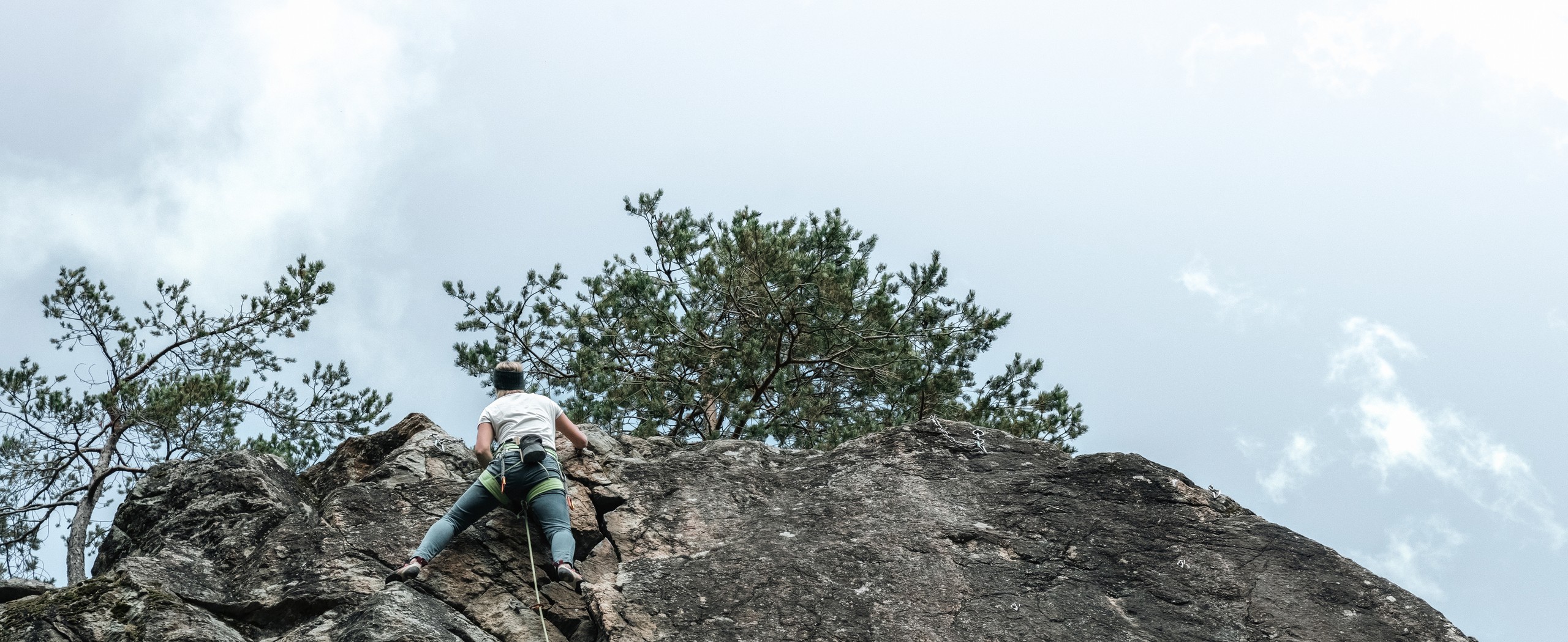 A person is climbing up a steep rock face outdoors beneath a bright sky.